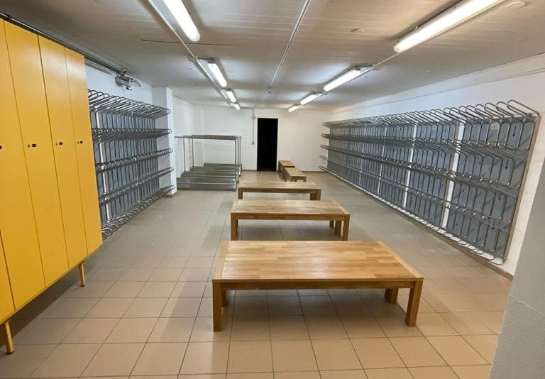 Skiaufbewahrung: Gelbe Schränke und Holzbänke in einem Lagerraum mit Skihalterungen. | Toptrock